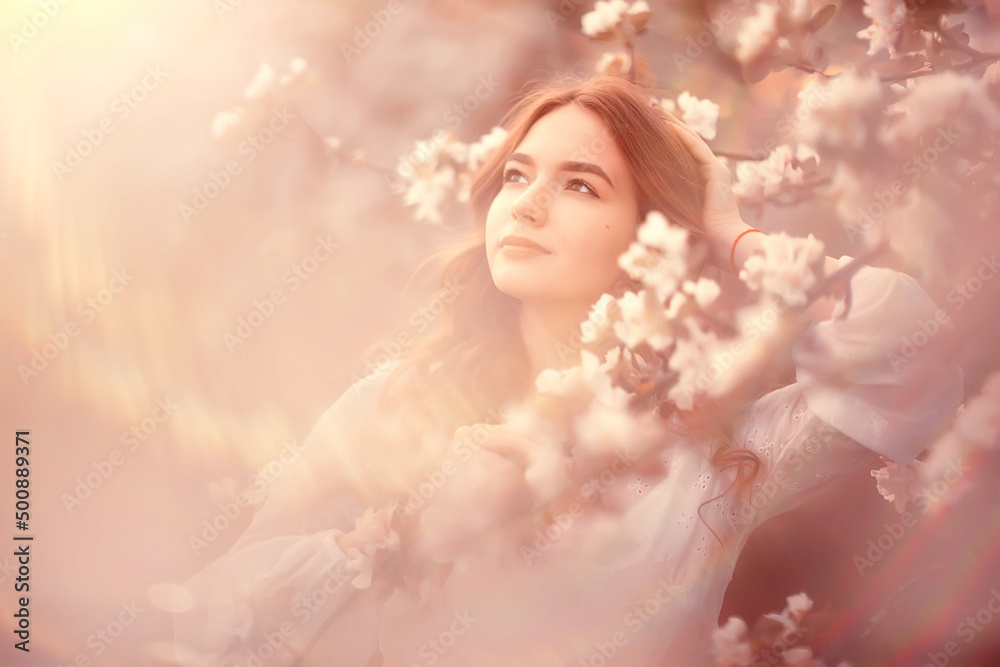 spring portrait of an adult happy woman in a blooming garden, sun rays and glare, april flowers girl