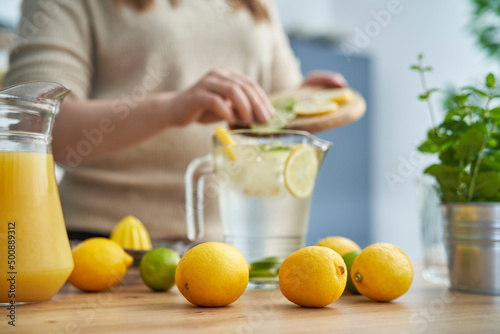 Lemons in the foreground and unrecognizable person making homemade lemonade with fresh