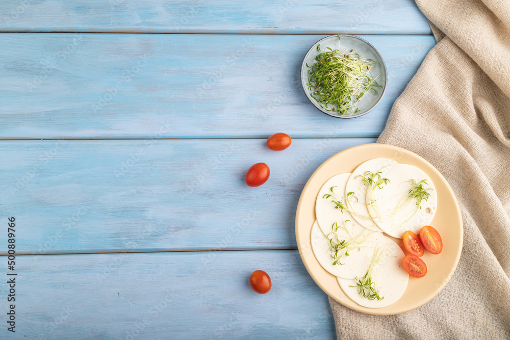 White cheese with tomatoes and cilantro microgreen on blue. top view, copy space.