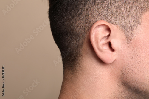 Man on beige background, closeup of ear. Space for text
