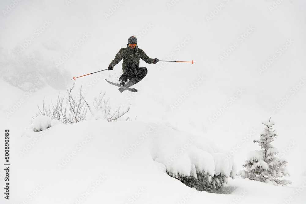 Shot of skier masterfully jumping in the air over a snow-covered mountain slope. Freeride skiing concept