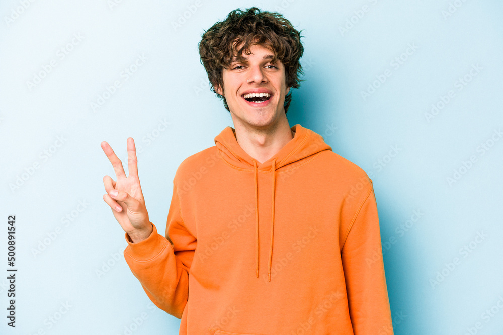 Young caucasian man isolated on blue background showing victory sign and smiling broadly. Young caucasian man isolated on blue background showing victory sign and smiling broadly.