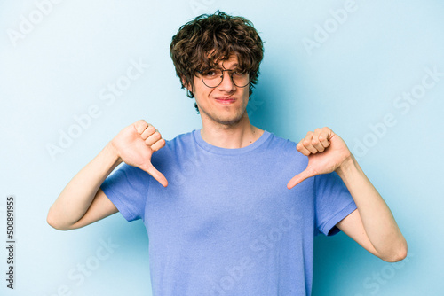 Young caucasian man isolated on blue background showing thumb down, disappointment concept.