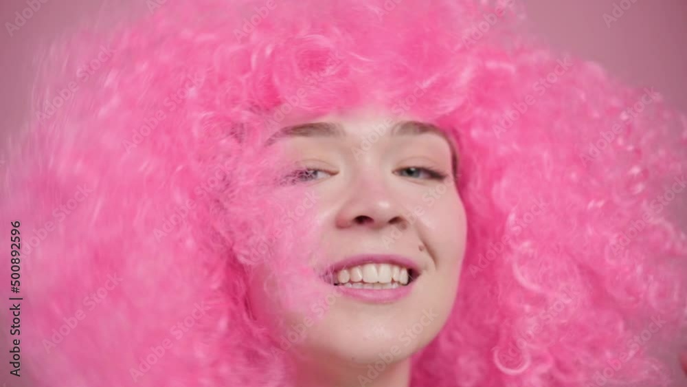 Smiling young pink haired woman waving hair on pink background, slow motion. Close up portrait. Smiling young pink haired woman waving hair on pink background, slow motion. Close up portrait.