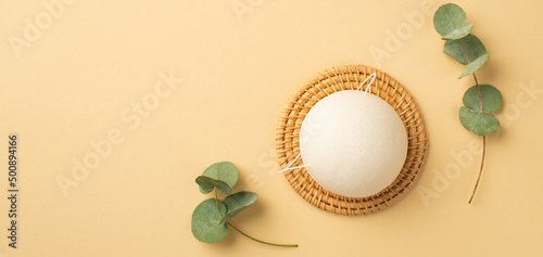 Top view photo of white konjac facial sponge on wicker stand and eucalyptus on isolated pastel beige background with copyspace photo