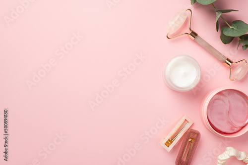 Skincare concept. Top view photo of rose quartz roller pink eye patches cream jar pink stylish barrettes scrunchy and eucalyptus on pastel pink background with blank space © ActionGP