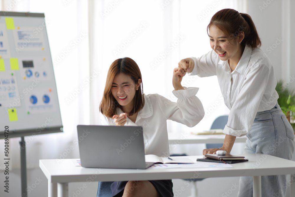 Asian woman and office colleague looking at laptop and showing excited expression. Asian woman and office colleague looking at laptop and showing excited expression.