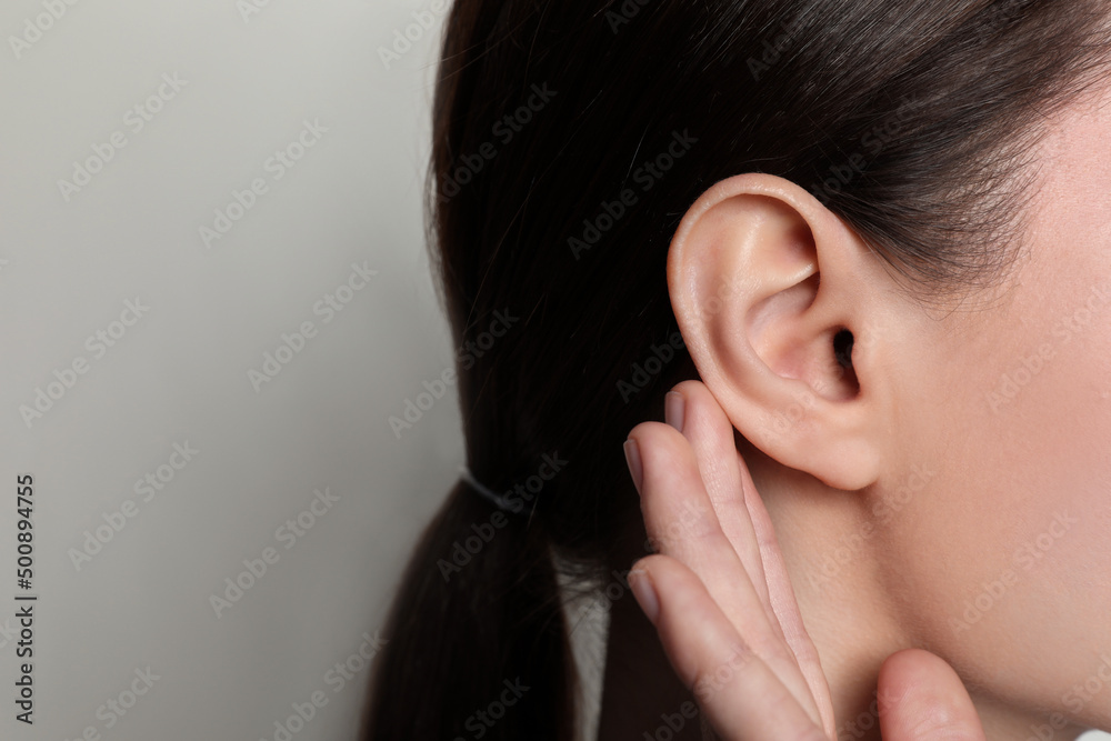 Woman showing hand to ear gesture on light background, closeup. Space for text - obrazy, fototapety, plakaty 