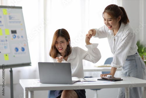 Asian woman and office colleague looking at laptop and showing excited expression. © Wasan