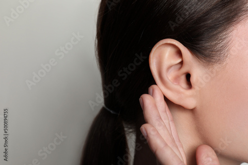 Fotobehang Woman showing hand to ear gesture on light background, closeup