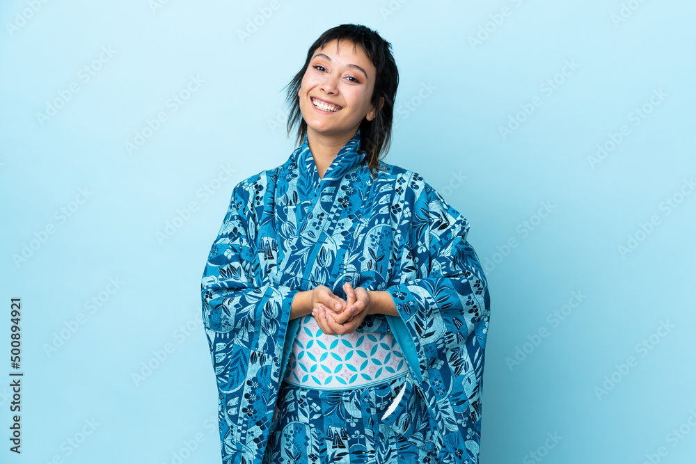 Young woman wearing kimono over isolated blue background laughing Young woman wearing kimono over isolated blue background laughing