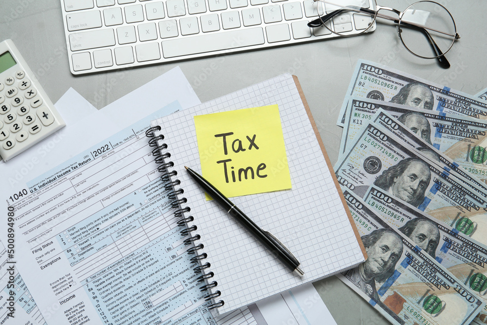 Reminder note with words Tax Time, documents, money and computer keyboard on grey table, flat lay Reminder note with words Tax Time, documents, money and computer keyboard on grey table, flat lay