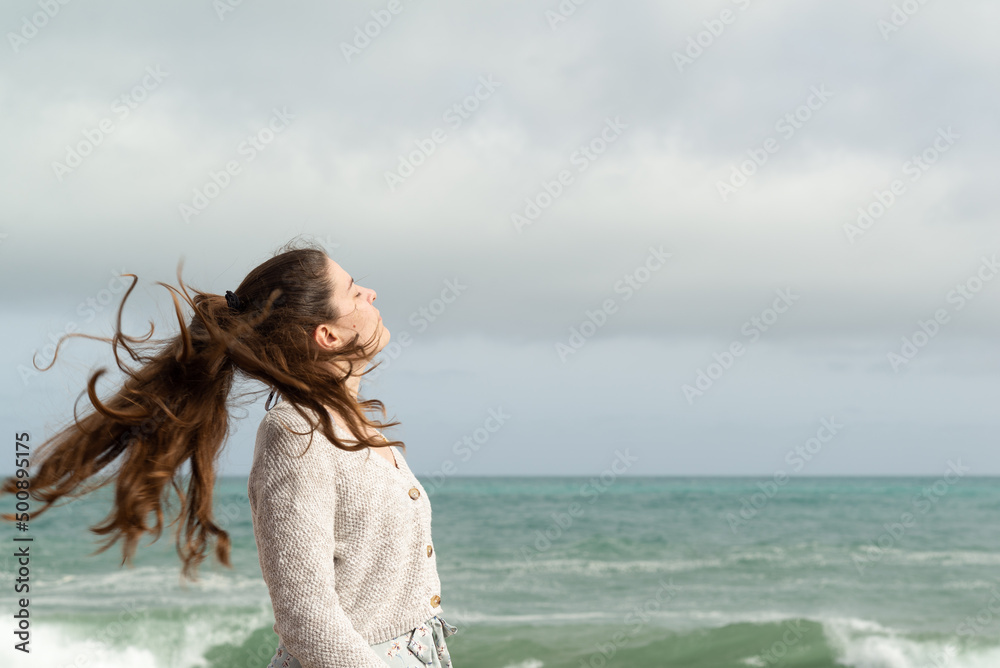 Obraz premium Young woman moving her long ponytail with the breeze of the sea. Inspirational concept.