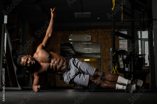 Shirtless african american man doing an elbow side plank in the gym.