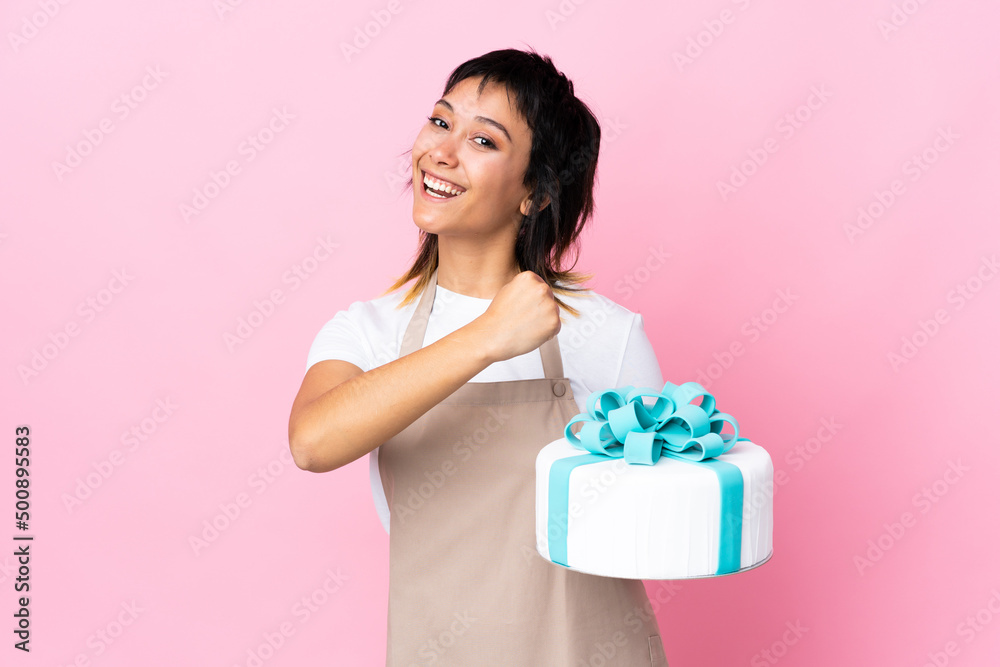 Uruguayan Pastry chef holding a big cake over isolated pink background celebrating a victory