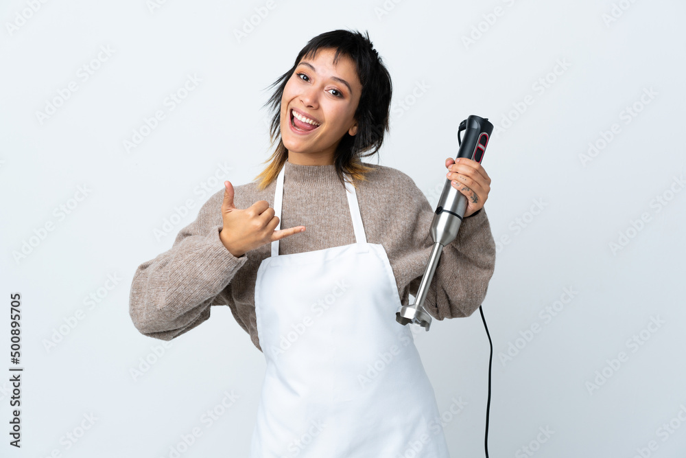 Chef Uruguayan girl using hand blender over isolated white background making phone gesture