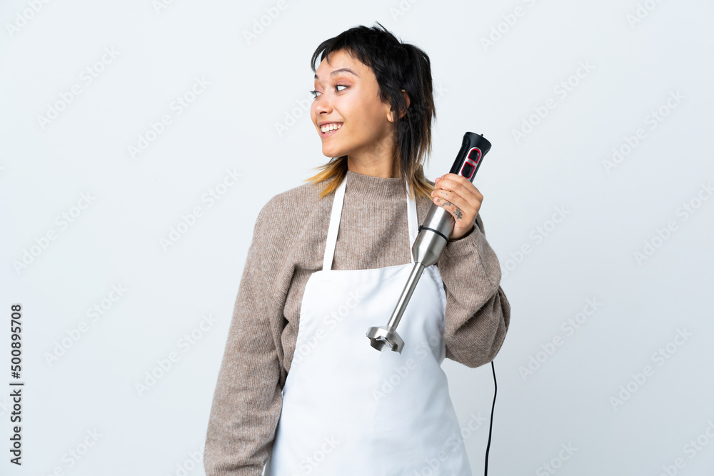 Chef Uruguayan girl using hand blender over isolated white background looking to the side Chef Uruguayan girl using hand blender over isolated white background looking to the side