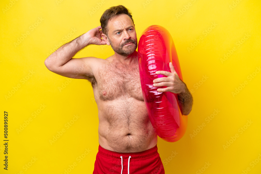 Middle age caucasian man holding inflatable donut isolated on yellow background having doubts