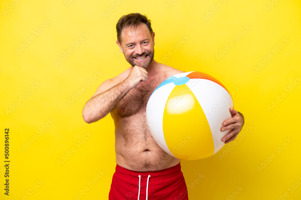 Middle age caucasian man holding beach ball isolated on yellow background celebrating a victory
