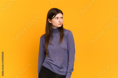 Young Ukrainian girl isolated on yellow background making doubts gesture looking side © luismolinero