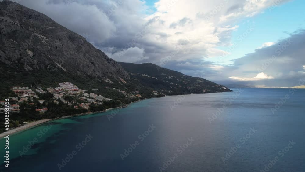 Panning shot, sideways from right to left of coastal line in greece. Green mountains and blue water with small houses visible and heavy clouds over the mountains. Panning shot, sideways from right to left of coastal line in greece. Green mountains and blue water with small houses visible and heavy clouds over the mountains.