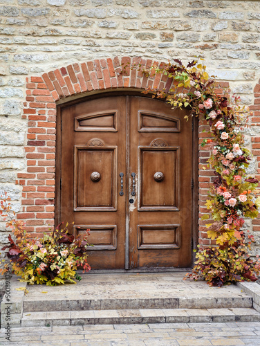 An old double door in a stone wall, decorated with flowers.
