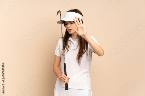 Young Ukrainian golfer girl isolated on beige background making stop gesture and disappointed