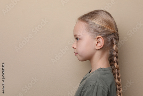 Profile portrait of cute little girl on beige background. Space for text photo