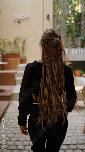 Fashionable pretty hippie woman with unusual dreads hairstyle, posing at city cafe, enjoying, toned colors. Young beautiful bohemian woman with blonde afro hairstyle dreads walking on the street .  © Roman