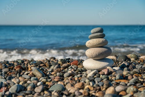 Beautiful pyramid of pebbles on the seashore with splashing waves on a sunny day  copy the space. Concept of balance  harmony