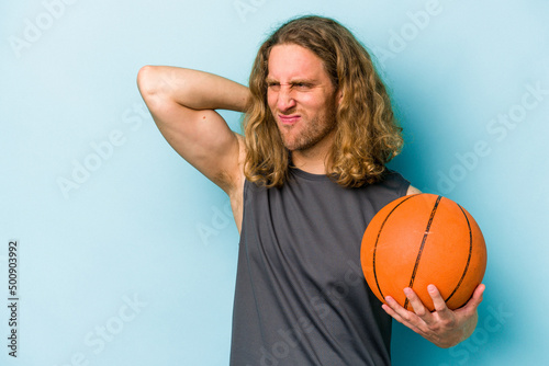 Young caucasian man playing basketball isolated on blue background touching back of head, thinking and making a choice.