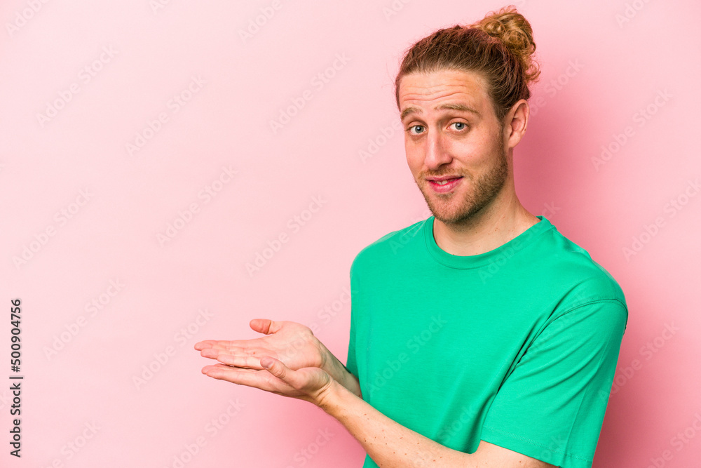Young caucasian man isolated on pink background holding a copy space on a palm. Young caucasian man isolated on pink background holding a copy space on a palm.