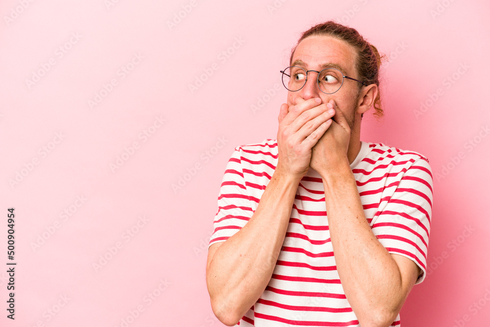 Young caucasian man isolated on pink background thoughtful looking to a copy space covering mouth with hand. Young caucasian man isolated on pink background thoughtful looking to a copy space covering mouth with hand.