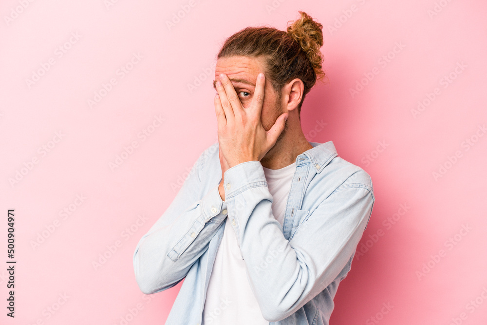 Young caucasian man isolated on pink background blink through fingers frightened and nervous. Young caucasian man isolated on pink background blink through fingers frightened and nervous.