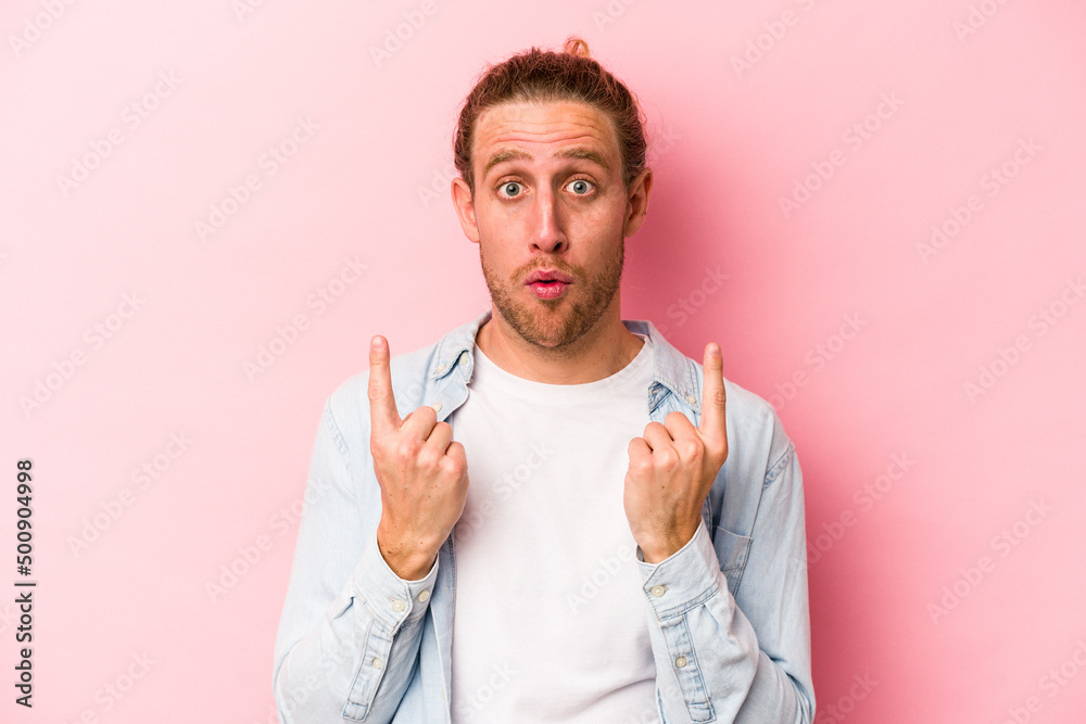 Young caucasian man isolated on pink background pointing upside with opened mouth. Young caucasian man isolated on pink background pointing upside with opened mouth.