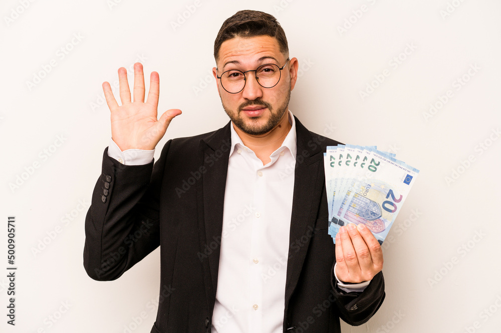 Business hispanic man holding banknotes isolated on white background smiling cheerful showing number five with fingers. Business hispanic man holding banknotes isolated on white background smiling cheerful showing number five with fingers.