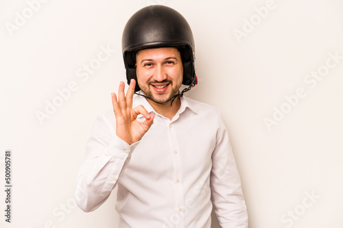 Hispanic business man going to work with motorcycle isolated on white background cheerful and confident showing ok gesture. © Asier