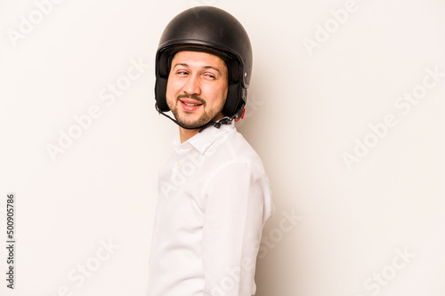 Hispanic business man going to work with motorcycle isolated on white background looks aside smiling, cheerful and pleasant.