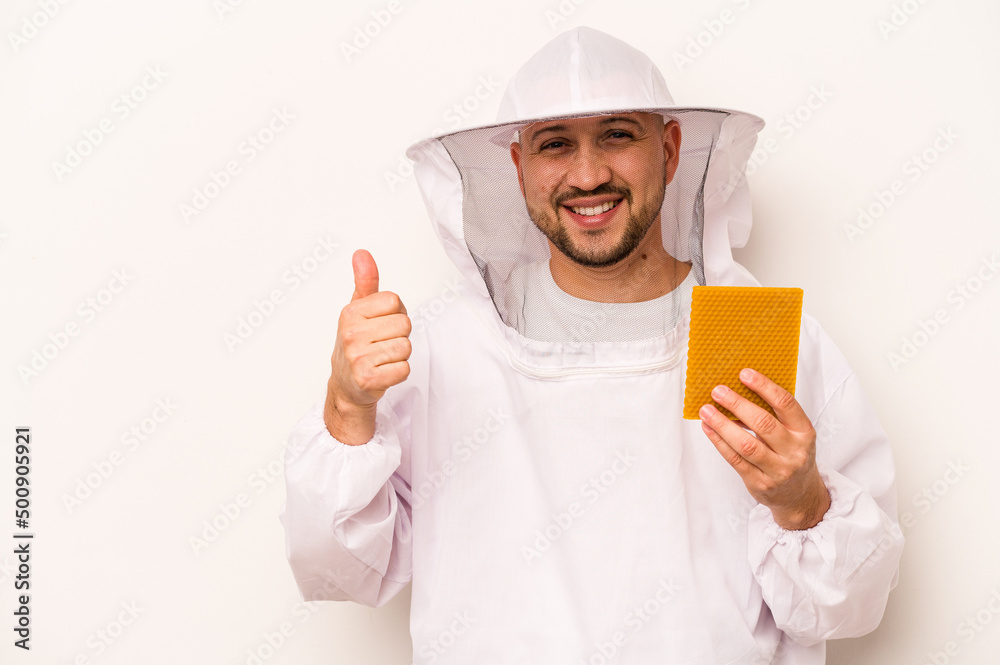 Hispanic beekeeper man holding honey isolated on white background smiling and raising thumb up Hispanic beekeeper man holding honey isolated on white background smiling and raising thumb up