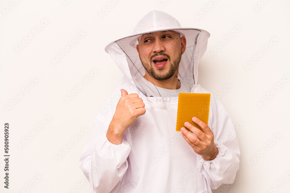Hispanic beekeeper man holding honey isolated on white background points with thumb finger away, laughing and carefree. Hispanic beekeeper man holding honey isolated on white background points with thumb finger away, laughing and carefree.
