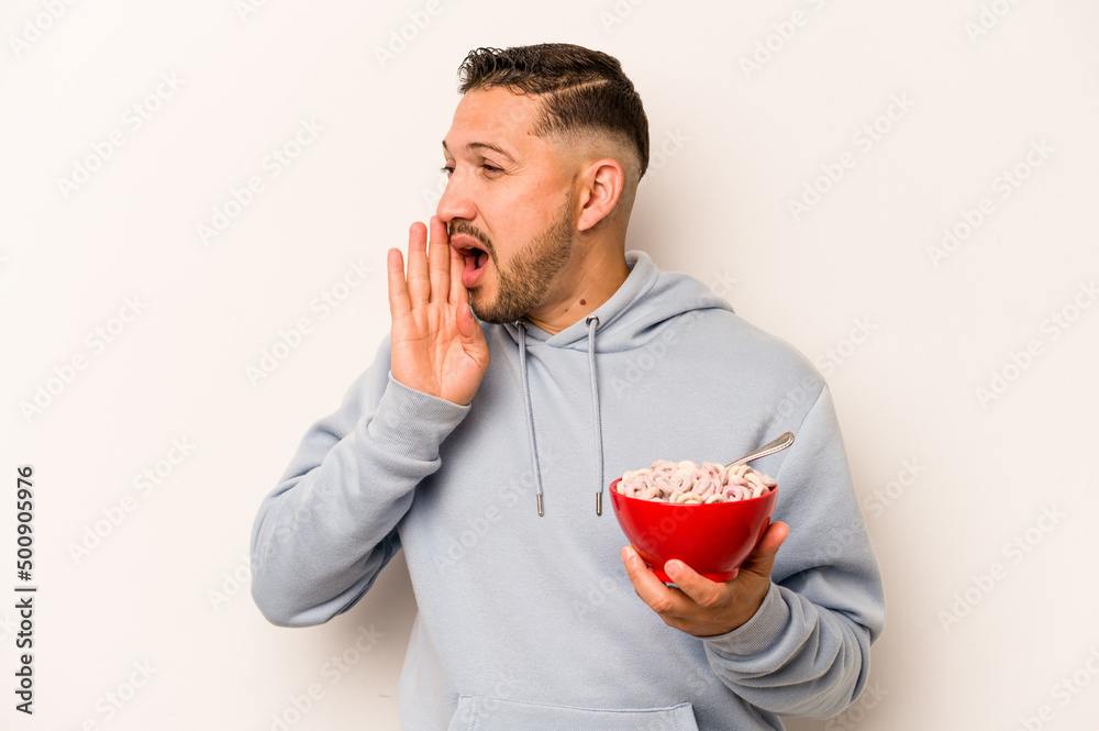 Hispanic man eating cereals isolated on white background shouting and holding palm near opened mouth. Hispanic man eating cereals isolated on white background shouting and holding palm near opened mouth.