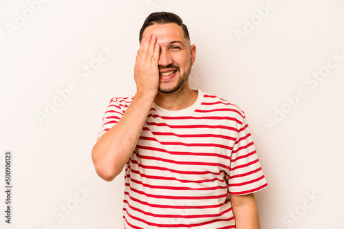 Young hispanic man isolated on white background having fun covering half of face with palm.