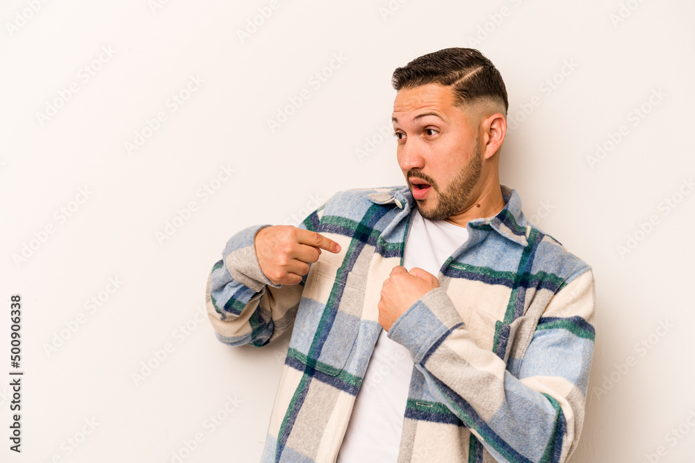 Young hispanic man isolated on white background surprised pointing with finger, smiling broadly.