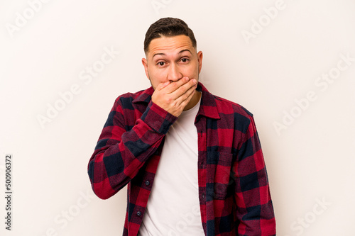 Young hispanic man isolated on white background covering mouth with hands looking worried.