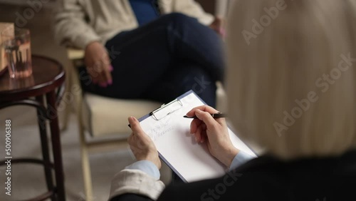 Close view of female psychologist is counseling client and writing during psychotherapy spbas. 4k Female psychotherapist listens to patient's story and holds clipboard in hand, takes notes and sits in photo