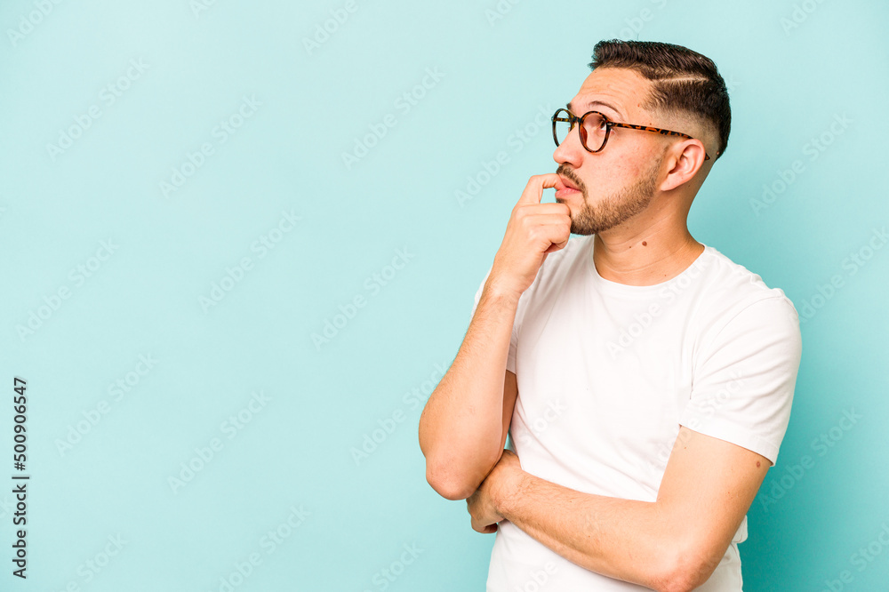 Young hispanic man isolated on blue background relaxed thinking about something looking at a copy space. Young hispanic man isolated on blue background relaxed thinking about something looking at a copy space.