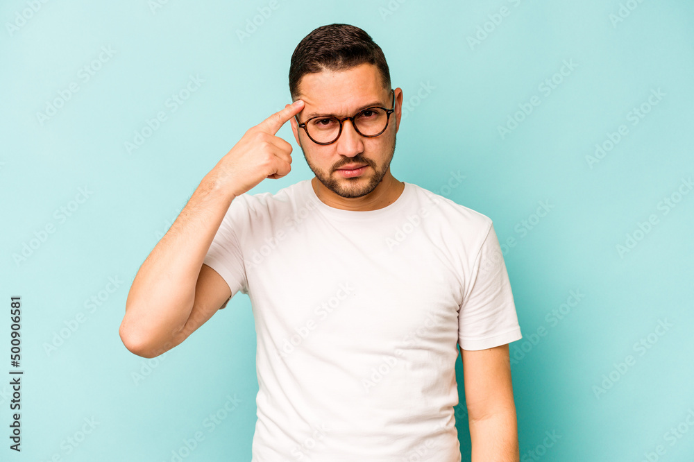 Young hispanic man isolated on blue background pointing temple with finger, thinking, focused on a task.