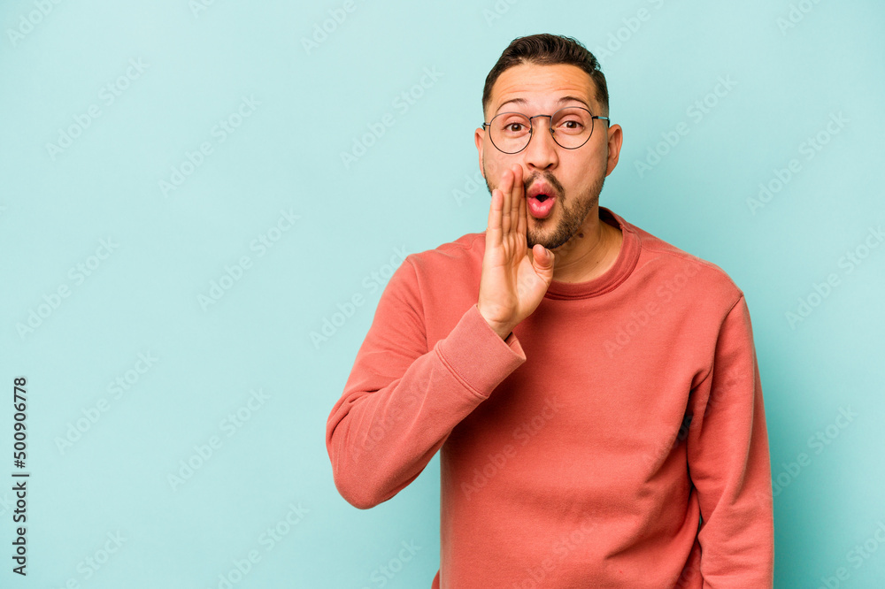 Young hispanic man isolated on blue background is saying a secret hot braking news and looking aside Young hispanic man isolated on blue background is saying a secret hot braking news and looking aside