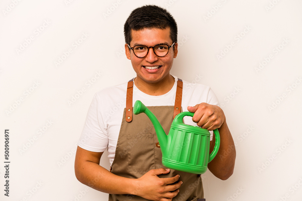 Young gardener hispanic man holding a watering can isolated on white background laughing and having fun. Young gardener hispanic man holding a watering can isolated on white background laughing and having fun.