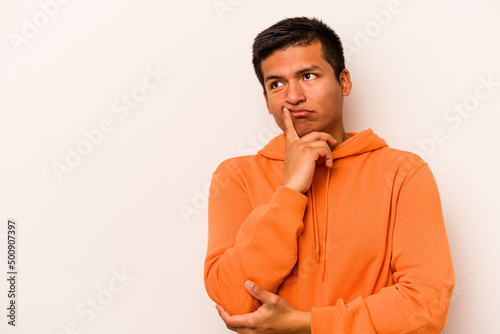 Young hispanic man isolated on white background looking sideways with doubtful and skeptical expression. © Asier